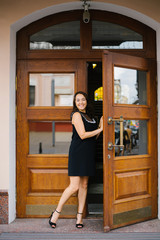 Smiling adult brunette woman in a dress before koloen leaves the building, stands in the wooden doors