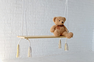 Teddy bear on a swing in the studio on a background of white brick.