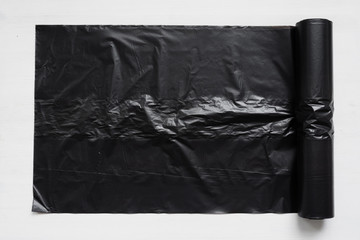 Black trash bag on a white wooden table background.