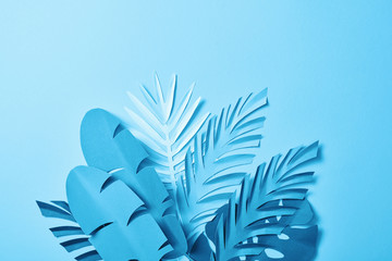 bunch of blue minimalistic paper cut palm leaves on blue background with copy space