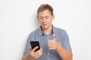 Daylight Portrait of young European Caucasian isolated on white background wearing blue shirt standing in front of camera, with phone in hand and smiling