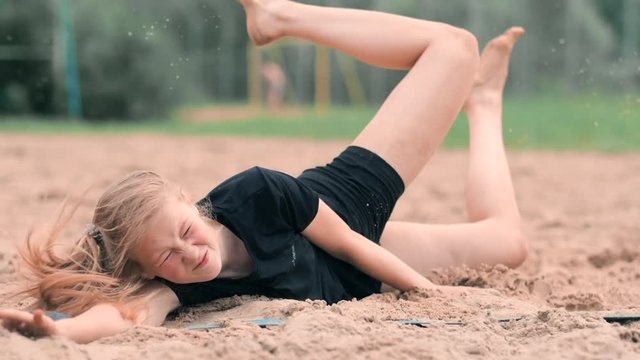 Young female athlete dives into the sand and saves a point during beach volleyball match. Cheerful Caucasian girl jumps and crashes into the white sand during a beach volley tournament