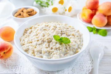 Oatmeal with apricot and nuts in bowl on white wooden table.