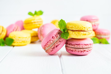Colorful macaroons and mint leaves on white wooden background.