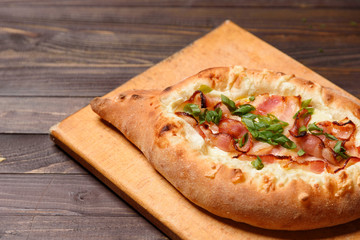 Georgian khachapuri with cheese and bacon on a dark wooden background