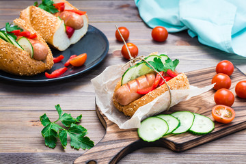 Appetizing hot dog made from fried sausage, rolls and fresh vegetables, wrapped in parchment paper on a cutting board on a wooden table