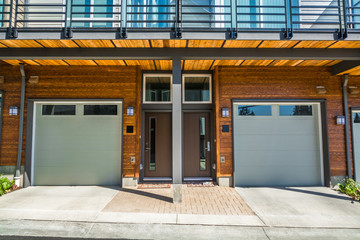 Gragage and entrance doors of brand new townhouses with wood finished wall on sunny day in British Columbia