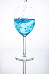 Blue cocktail is poured into a glass on a white background with reflection, splashes and bubbles
