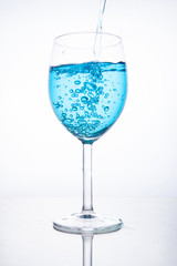 Blue cocktail is poured into a glass on a white background with reflection, splashes and bubbles