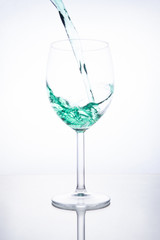 Green cocktail is poured into a glass on a white background with reflection, splashes and bubbles