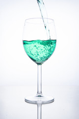 Green cocktail is poured into a glass on a white background with reflection, splashes and bubbles
