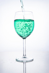 Green cocktail is poured into a glass on a white background with reflection, splashes and bubbles