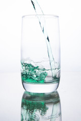 Green cocktail is poured into a glass on a white background with reflection, splashes and bubbles