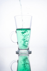 Green cocktail is poured into a glass on a white background with reflection, splashes and bubbles