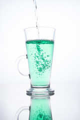 Green cocktail is poured into a glass on a white background with reflection, splashes and bubbles