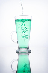 Green cocktail is poured into a glass on a white background with reflection, splashes and bubbles