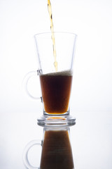 Dark beer is poured into a mug on a white background.