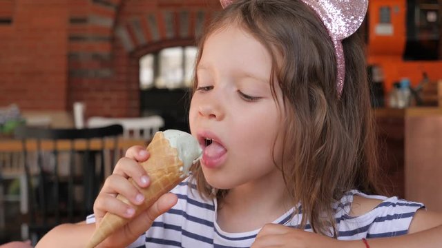 Little kid girl closeup portrait face eating licking ice cream cone with pleasure