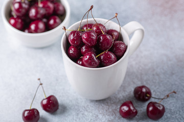 Fresh ripe red cherries in a white mug on a gray stone background Closeup Water drops Top view