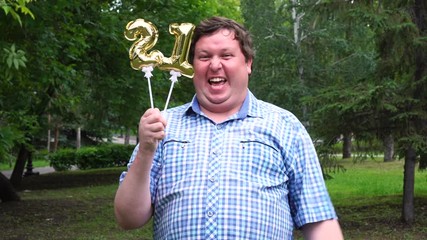 Big man holding golden balloons making the 21 number outdoor. 21th anniversary celebration party