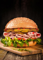 sandwich with sausage, cucumber, tomato and lettuce leaves on wooden background