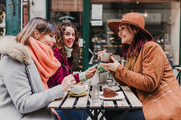 Three women friends having coffee in a terrace in Oporto, Portugal. Having a fun conversation. Lifestyle, tourism and holidays