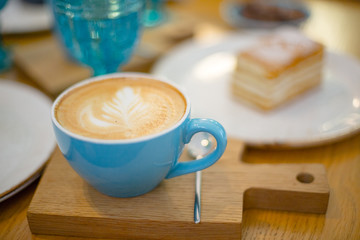 Slice of sweet tasty Honey Cake Medovik and blue cup of cappuccino on the wooden table