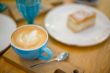 Slice of sweet tasty Honey Cake Medovik and blue cup of cappuccino on the wooden table