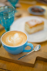 Slice of sweet tasty Honey Cake Medovik and blue cup of cappuccino on the wooden table
