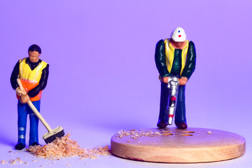 Conceptual image of miniature figure workmen making holes in wooden sewing buttons