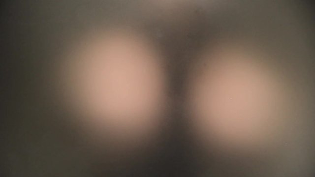 Unrecognizable scary and naked man looking behind a frosted glass carefully.