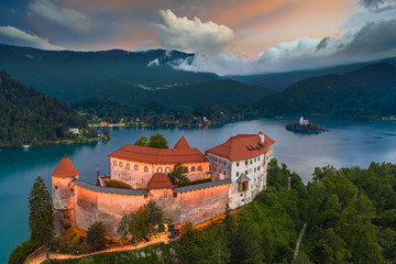 Fototapeta na wymiar Bled, Slovenia - Aerial view of beautiful illuminated Bled Castle (Blejski Grad) with the Church of the Assumption of Maria and Julian Alps at background at blue hour with dramatic sky