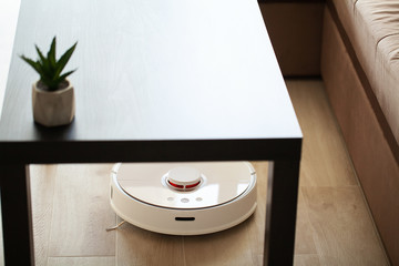 Smart House. Vacuum cleaner robot runs on wood floor in a living room.