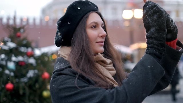Woman take photo on Christmas tree decoration . A beautiful young woman or girl doing selfie or using phone emotionally outdoors in front of Christmas holidays decorations.