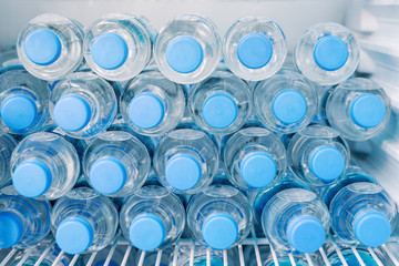 Rows of many transparent plastic bottles with drinking water supply in white refrigerator. Mineral...