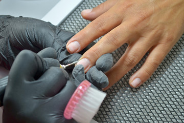 Master of manicure in black gloves and with a brush makes hardware manicure by nail cutter, top view