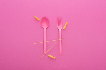 Obraz na płótnie Canvas pink plastic spoon and fork and two different kinds of pasta isolated on pink