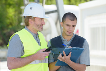 two male builders working over clipboard outdoors