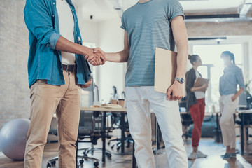 Two young male colleagues shaking hands in office