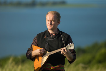 A man in traditional russian clothes playing balalaika on the field