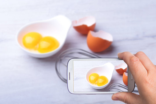 hands of man with smartphone taking photo egg yolk. ingredient for homemade tiramisu cake in close up.