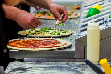 Cook in the kitchen putting the ingredients on the pizza. Production and delivery of food.