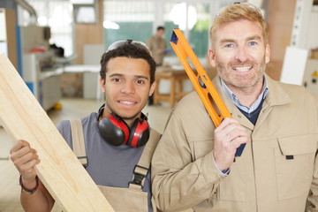 carpenter holding spirit level with apprentice in workshop