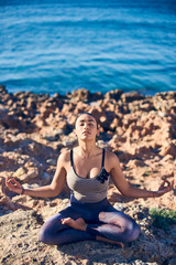 Calm young woman meditating at the beach against a beautiful blue sea.