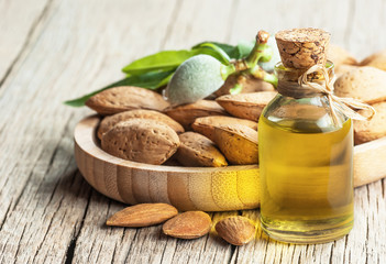 Glass bottle of Almond oil and almond nuts, almonds with shell in bamboo bowl on wooden backdrop...