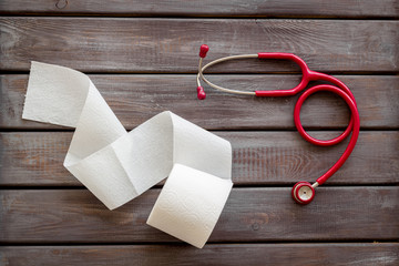 Proctology concept with toilet paper roll and stethoscope on wooden background top view