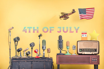 Retro microphones, wooden plane and USA flag, old radio, calendar, star front yellow background with 4th of July date text. Independence day congratulations greeting card. Vintage style filtered photo