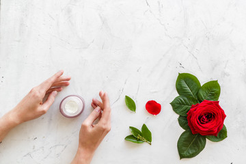 Obraz na płótnie Canvas Cosmetic spa set with rose flowers and cream for body in hands on white marble desk background top view mockup