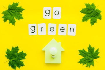 Go green text with house toy, lamp, green maple leaves on yellow background top view