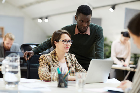 Portrait of young African business intern using laptop with female colleague while working in office, copy space
